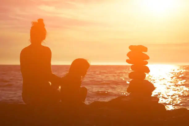 Mother and daughter enjoying sunset on a coast near zen-stones.