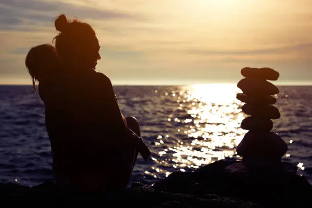 Mother and daughter enjoying sunset on a coast near zen-stones.