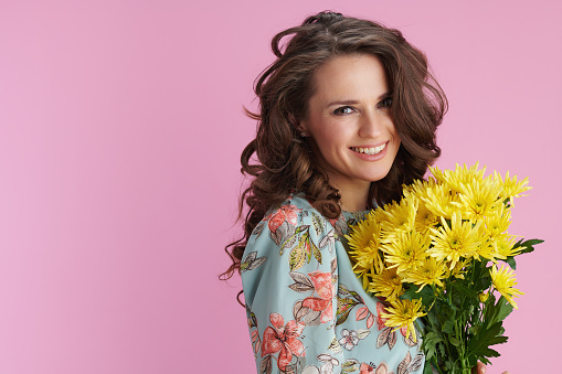 Portrait of smiling modern female in floral dress with yellow chrysanthemums flowers isolated on pink background.