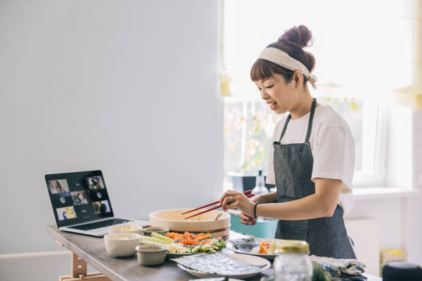 Woman cooking food while making a video call Japanese woman cooking food and attending video call at home cooking class photos stock pictures, royalty-free photos & images