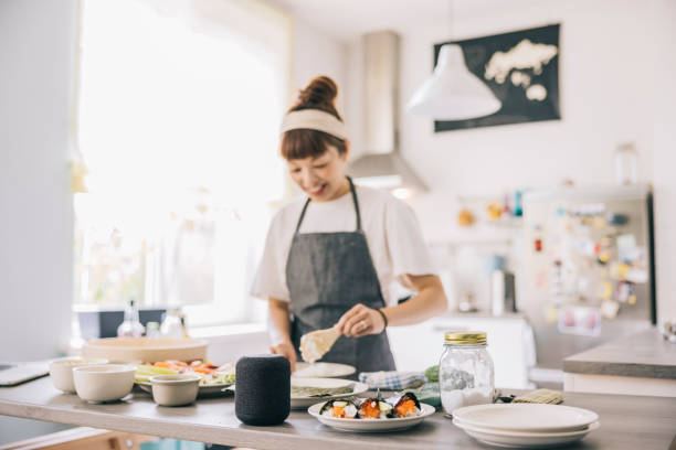 Woman using virtual assistant while cooking Japanese woman using smart speaker, while cooking at home. virtual assistant stock pictures, royalty-free photos & images