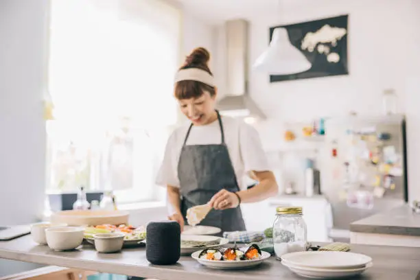 Japanese woman using smart speaker, while cooking at home.