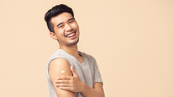 Portrait of Asian man showing his shoulder with bandage after getting a vaccination during covid-19 immunization program.