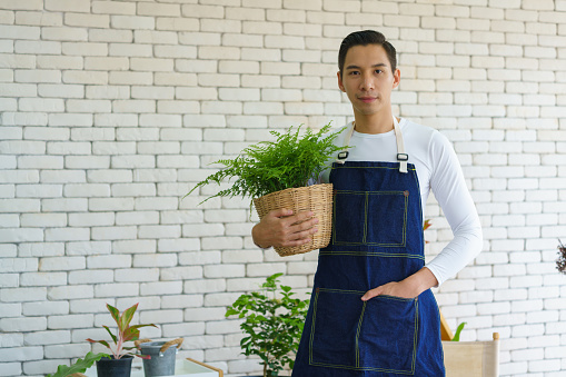 Portrait of entrepreneur gardener in apron holding a rattan basket plant pot at the floral shop. Florist plant seller, Botanist working in garden nursery. Ecommerce shopping, Small business and Hobby.