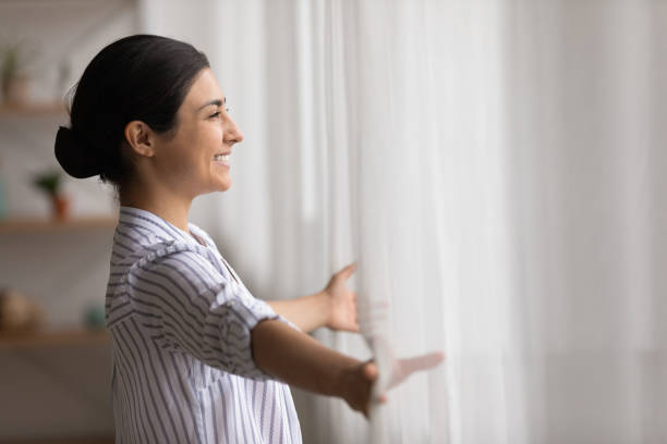 mujer india sonriente mira en la ventana soñando - new possibilities fotografías e imágenes de stock