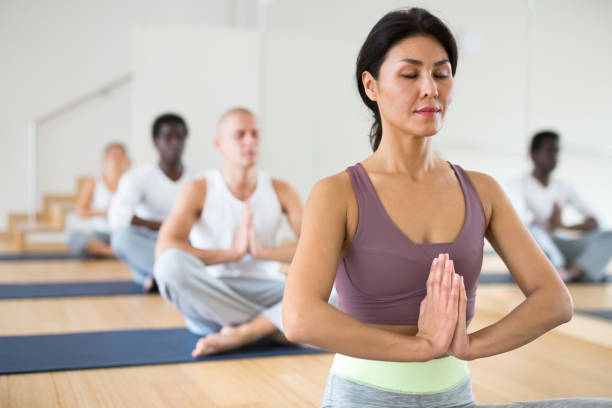 Two women meditating on a yoga mat with copy space. Young people sitting on the floor practicing mediation by doing the lotus pose feeling calm and at peace inside a bright and quiet wellness center