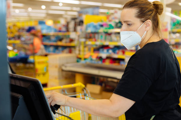 Woman in a supermarket at a self-checkout counter shopping in medical mask, Covid security, city life Woman in a supermarket at a self-checkout counter shopping in a medical mask, Covid security, city life self checkout photos stock pictures, royalty-free photos & images