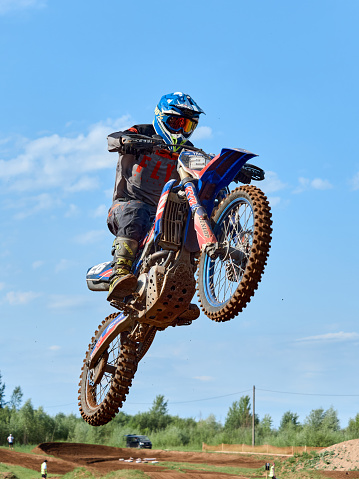 Racer on a cross-country motorcycle in sports equipment in flight after jumping on a springboard, against the blue sky. Kirov, Russia - June 20, 2021