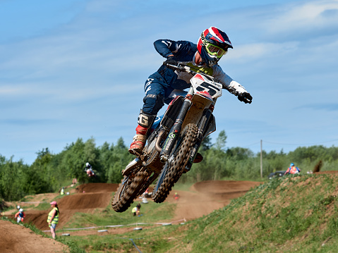 Racer on a cross-country motorcycle in sports equipment in flight after jumping on a springboard, against the blue sky. Kirov, Russia - June 20, 2021