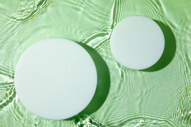 istock Two empty white circle podium on transparent green water background 1325398389