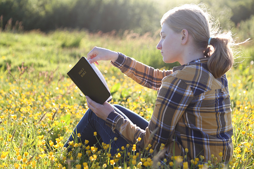 Young girl reading bible in the meadow