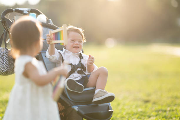 12 year old boy next to his younger baby brother sleeping in a green stroller in a spring park.