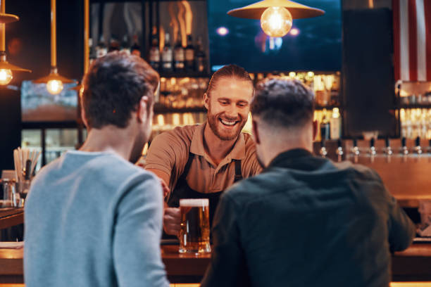 istock Cheerful bartender serving beer to young men 1325402614