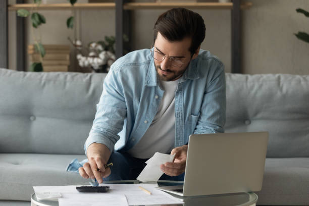 istock Concentrated young 30s man in eyeglasses calculating expenditures. 1325412549