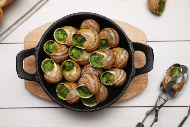 istock Delicious cooked snails served on white wooden table, flat lay 1325415216