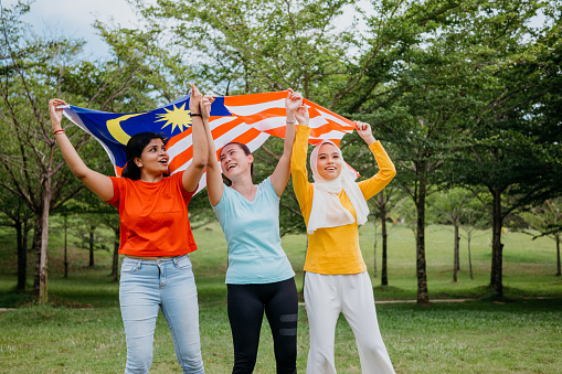 Image of malaysian multi racial girls holding national flag for independence day celebration at public park
