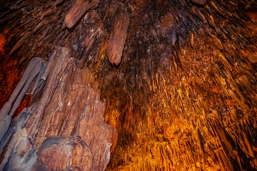 Natural texture of the Damlatas cave ceiling with many stalactites (Alanya, Turkey). Brown-orange-yellow pattern of spiky conical mineral formations on the surface underground