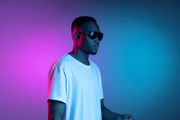 istock Young african man in sunglasses posing in neon light on gradient background. Concept of emotions, facial expression. 1325418427