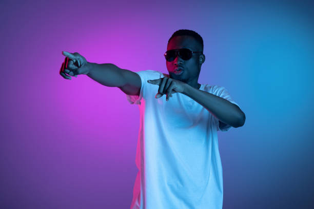 istock Young african man in sunglasses posing in neon light on gradient background. Concept of emotions, facial expression. 1325418434