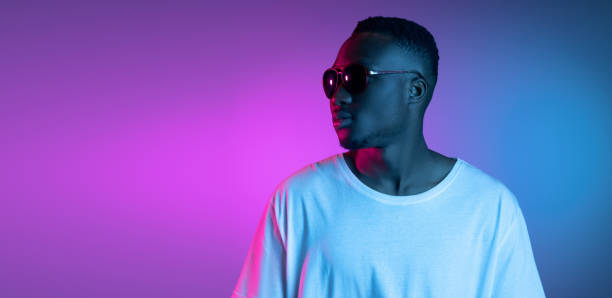 istock Young african man in sunglasses posing in neon light on gradient background. Concept of emotions, facial expression. 1325418436