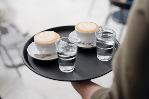 Anonymous Waiter Carries the Two Cappuccino and Two Glasses of Water on a Serving Tray
