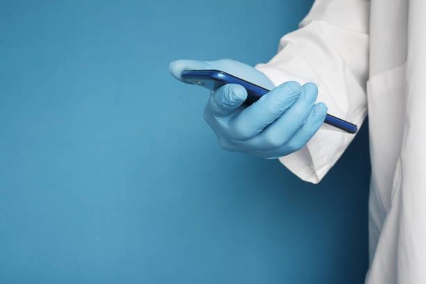 istock doctor's hand in protective gloves using a smartphone against blue background 1325420630