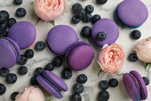 Delicious macarons, blueberries and flowers on white marble table, flat lay