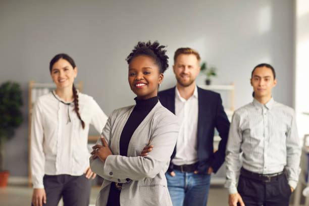 empresaria afroamericana con los brazos cruzados y sonriendo con el equipo de trabajadores detrás - fundador fotografías e imágenes de stock