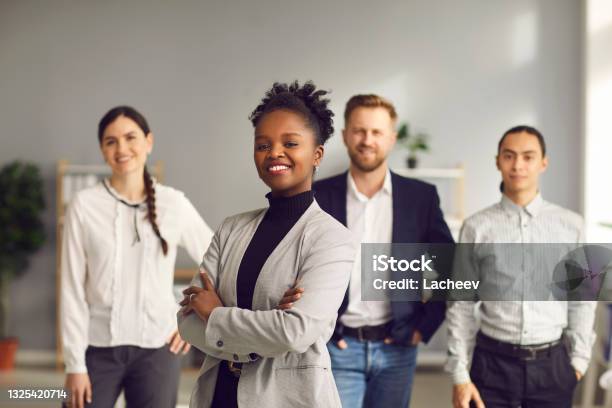 Africanamerican Businesswoman Standing Arms Folded And Smiling With Team Of Workers Behind Stock Photo - Download Image Now