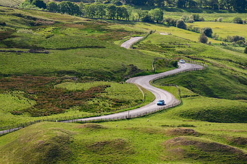 Bucolic rural scene of car on journey through Englands Peak District travelling along an s shaped curved road.