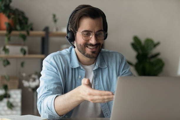 istock Happy young man in headset holding web camera video meeting. 1325421010