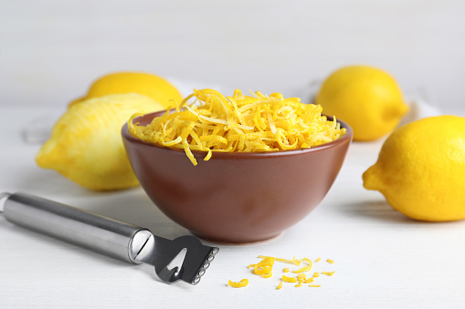 Brown bowl with fresh lemon zest on white table