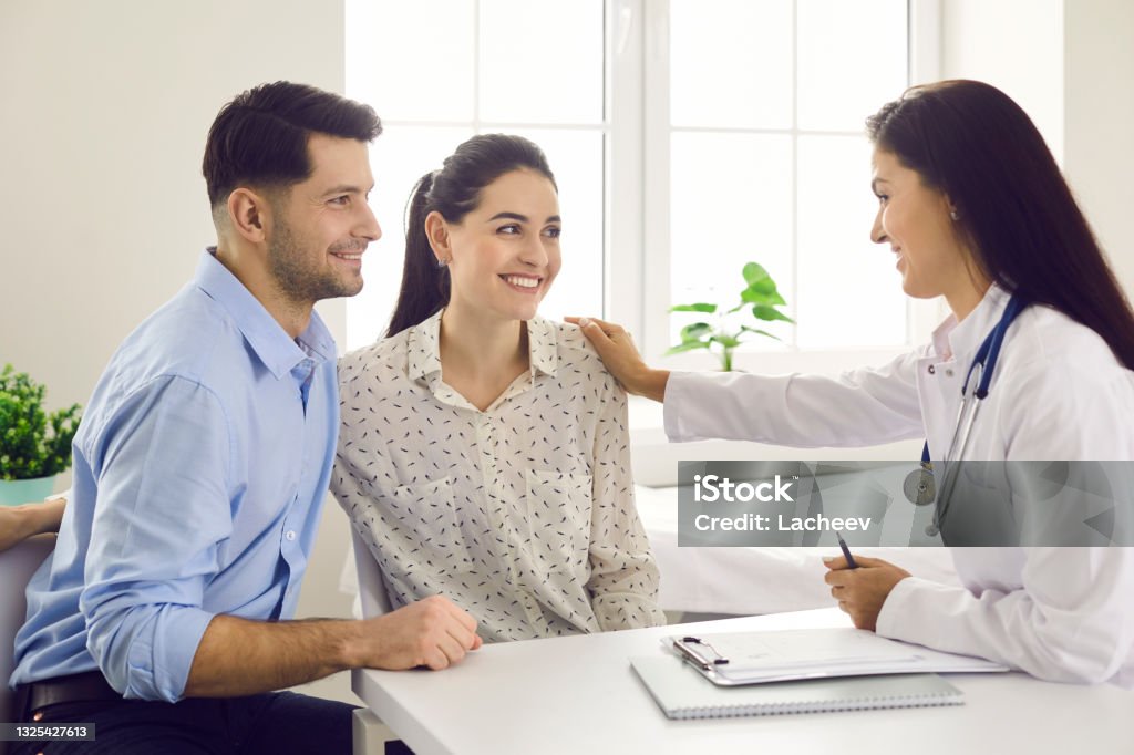 Female doctor consulting young couple patients in fertility clinic about IVF or IUI. Female doctor consulting young couple patients in fertility clinic about IVF or IUI. Doctor encourages and assures the young couple that everything will be fine. Concept of artificial insemination. Doctor Stock Photo