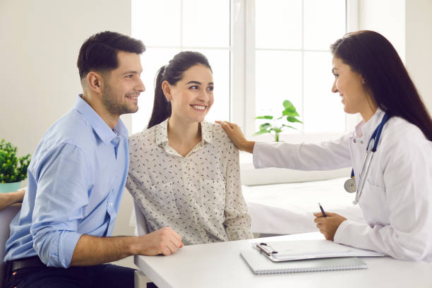 Female doctor consulting young couple patients in fertility clinic about IVF or IUI. stock photo