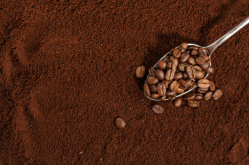 Coffee beans on spoon on ground coffee background. Closeup.