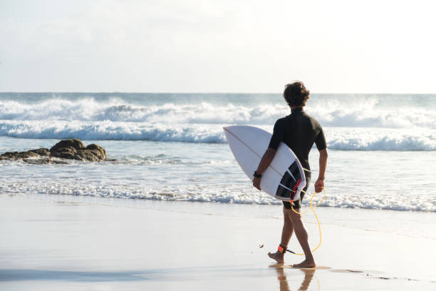 istock Unrecognizable young surfer walking by the beach shore 1325432007