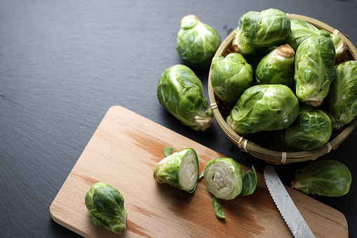 Fresh organic brussels sprouts raw on a cutting board with black stone table, top view.