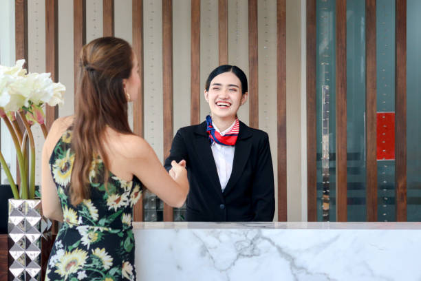 Happy smiling young beautiful Asian female receptionist in suit shaking hands with customer at hotel reception counter desk, check in hotel service on vacation concept. Happy smiling young beautiful Asian female receptionist in suit shaking hands with customer at hotel reception counter desk, check in hotel service on vacation concept. hotel occupation concierge bell service stock pictures, royalty-free photos & images