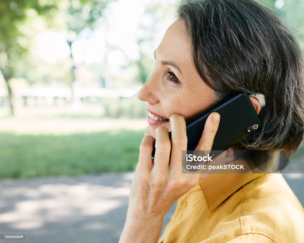 Mature woman with hearing aid has a full life and can hear interlocutor on phone. Hearing solution and innovation technology Ear Stock Photo