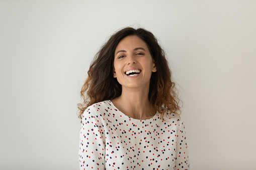 Head shot portrait of laughing excited woman standing isolated on grey background, overjoyed attractive young female with curly hair looking at camera, having fun, natural beauty, healthy smooth skin