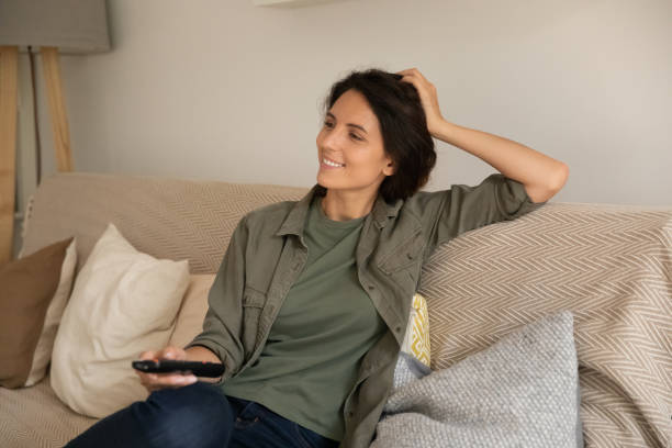 istock Smiling woman holding remote controller, watching tv, relaxing on couch 1325452761