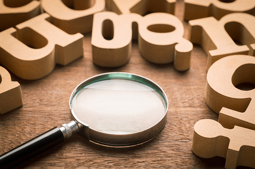 Magnifying glass on wood table with many thick wood English alphabets, English communication, glossary concept