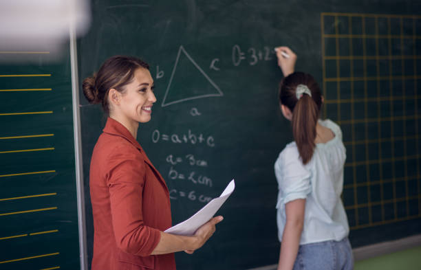 Student or teacher standing in front of the blackboard. Young girl raised her hand and volunteered to solve math problem in front of her classmates. She loves mathematics, especially geometry, and today she got to calculate circumference of a triangle. Math Aptitude Test stock pictures, royalty-free photos & images