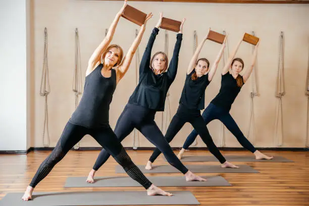Photo of Group of women practicing yoga stretching using wooden blocks, exercise for spine and shoulders flexibility