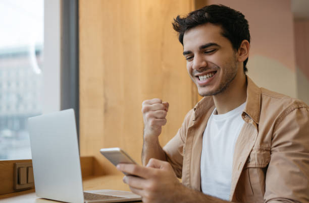 Handsome Indian man holding mobile phone, communication, receive text message, reading good news. Asian business man with happy emotional face celebration success, sitting in modern office