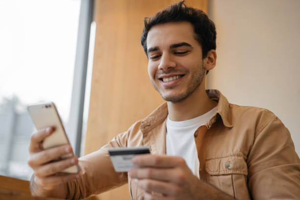 istock Handsome Indian man holding credit card, using smartphone for online shopping, mobile banking. Young asian freelancer receive payment. Happy emotional hipster ordering food online, booking tickets 1325466021