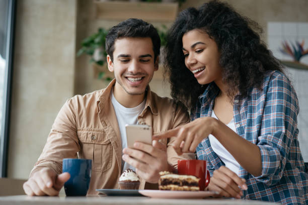 온라인 쇼핑을위한 휴대 전화 응용 프로그램을 사용하여 행복한 커플. 감성적인 친구 커뮤니케이션, 웃음, 디지털 스크린 보기, 카페에 함께 앉아 - mobile phone telephone couple women 뉴스 사진 이미지