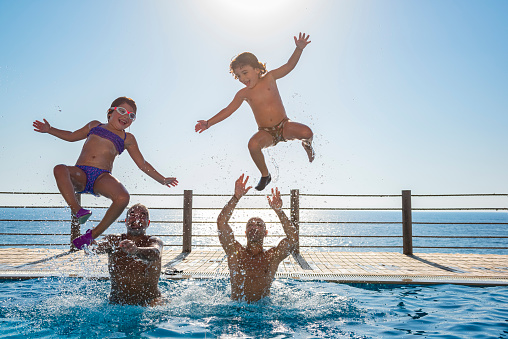 Two Happy Kids with Their Fathers Having Fun in the Pool. Jumping and Making Splashes. Enjoying Summer Holidays on the Beach Resort.