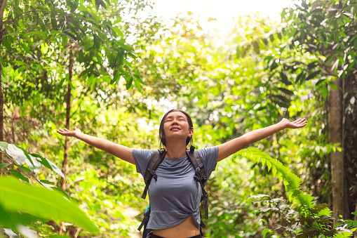 Portrait of cheerful young female hiker jungle trekking in tropical rainforest, arms outstretched for freedom, enjoying the connection with nature