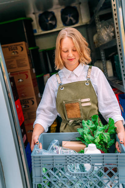 Portrait of a Happy Young Caucasian Woman Standing at the Door of a Walk-In Refrigerator Holding a Basket of Delicious, Healthy, Organic Produce at a Local Small Business Farm-to-Table Supplier in Colorado retrato de una joven y feliz mujer caucásica de pie en la puerta de un refrigerador sin cita previa sosteniendo una cesta de productos deliciosos, saludables y orgánicos en un proveedor local de la granja a la mesa de una pequeña empresa en colorado